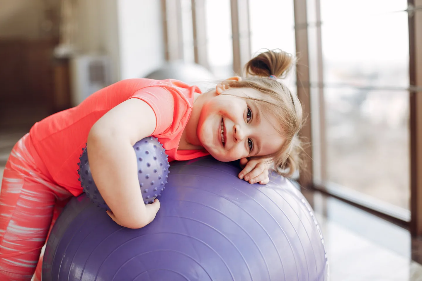 Criança em atividade terapêutica com bola de exercício durante sessão de fisioterapia neurológica infantil